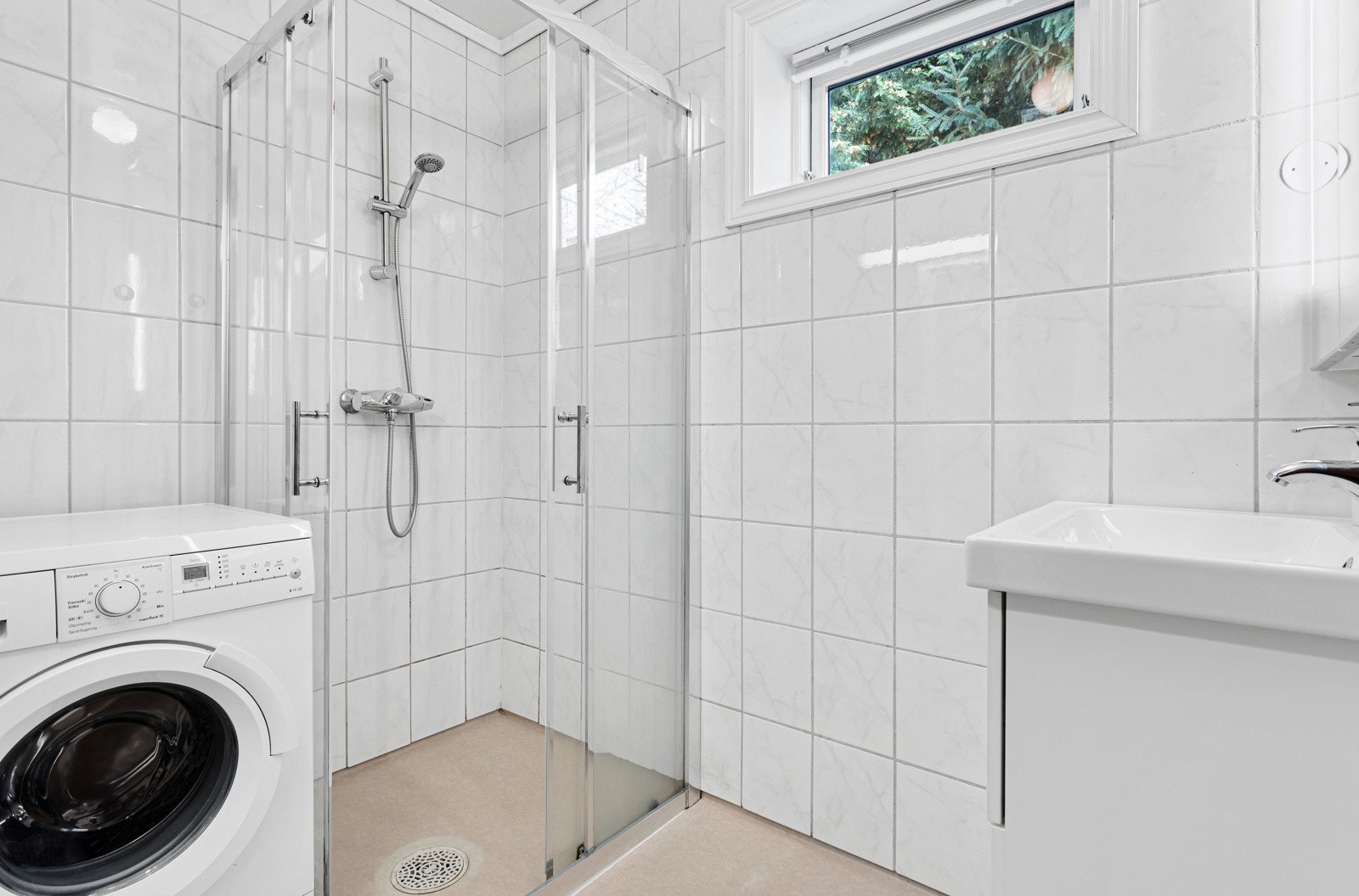 Baderom er utstyrt med dusjhjørne, servant i innredning og opplegg for vaskemaskin. Galleribilde