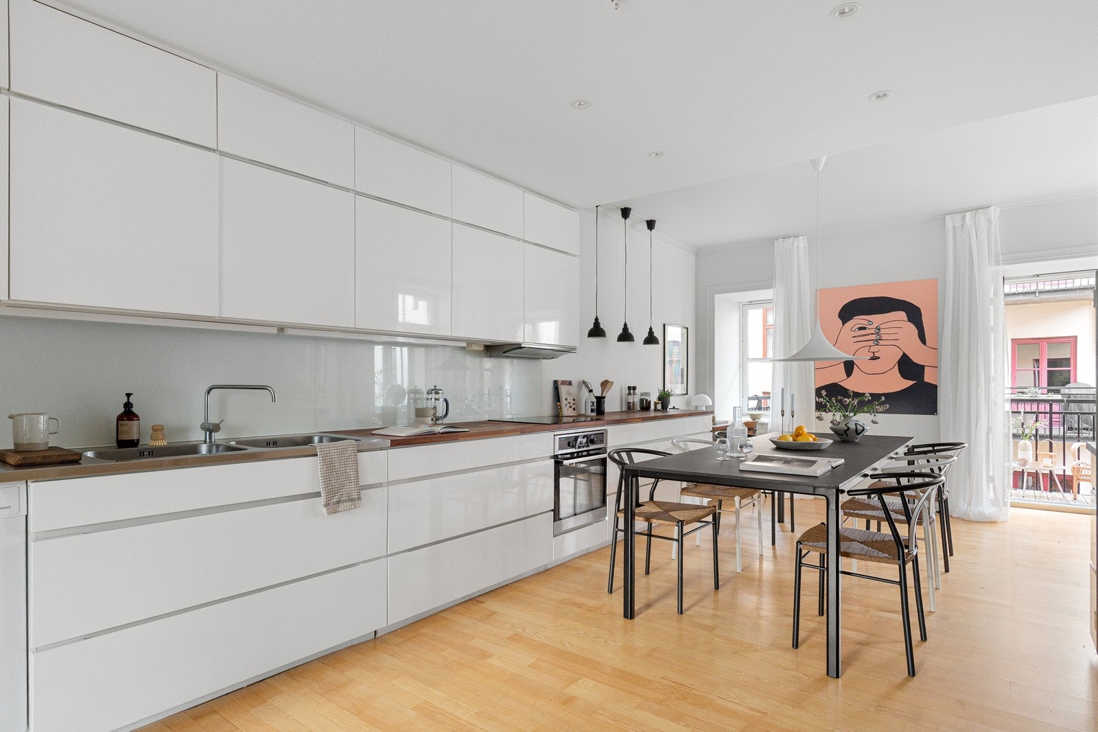 Innholdsrik kjøkkeninnredning med hvite greps frie høyglans fronter. Overskap med benkebelysning og glassplater på vegg Galleribilde