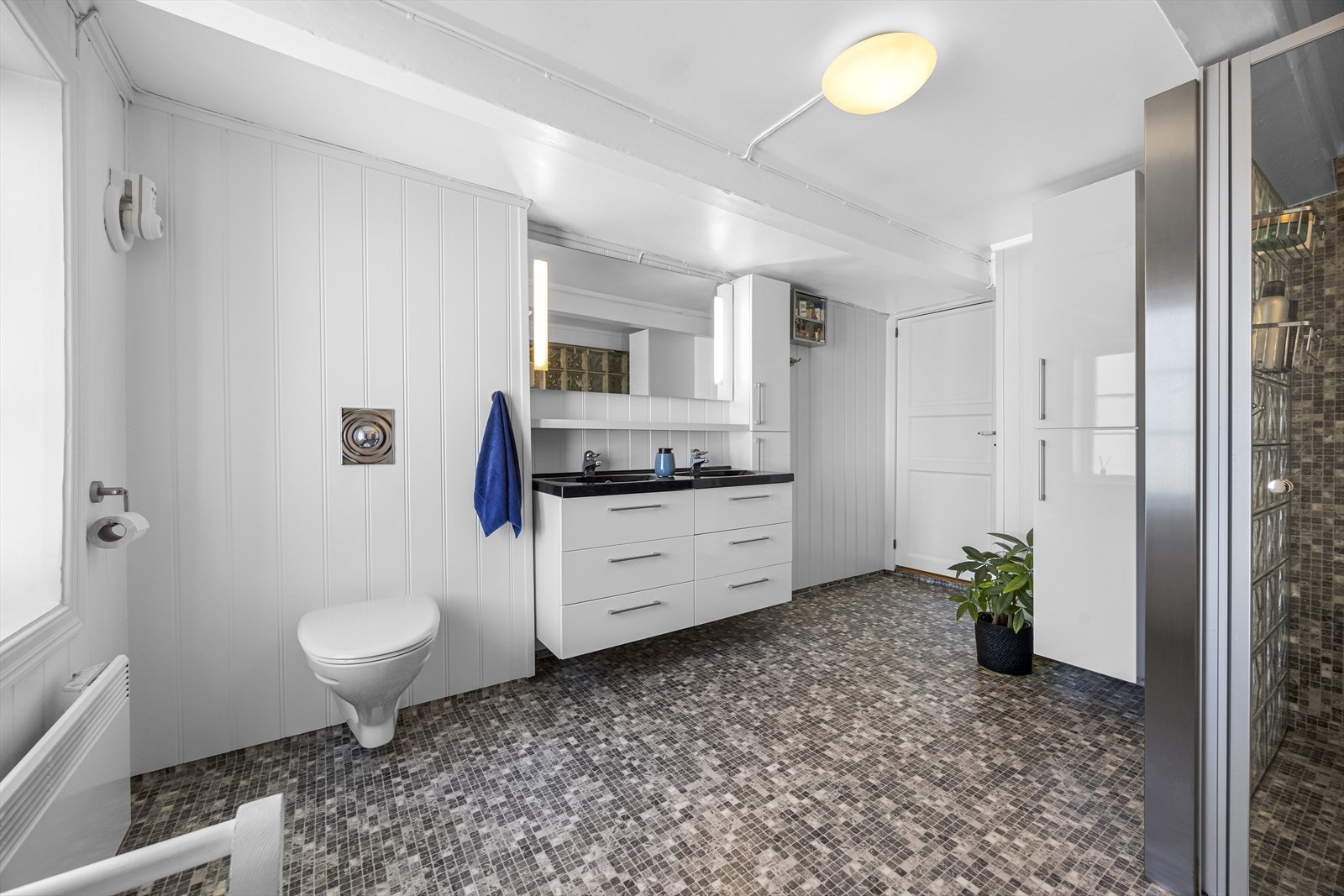 Stort og godt bad med belegg på gulv og i dusjnisje, malt mdf på resten av veggene. Badet er innredet med baderomsinnredning med speil, vegghengt wc, stor dusjnisje og innhuk til vaskemaskin og tørketrommel. Galleribilde