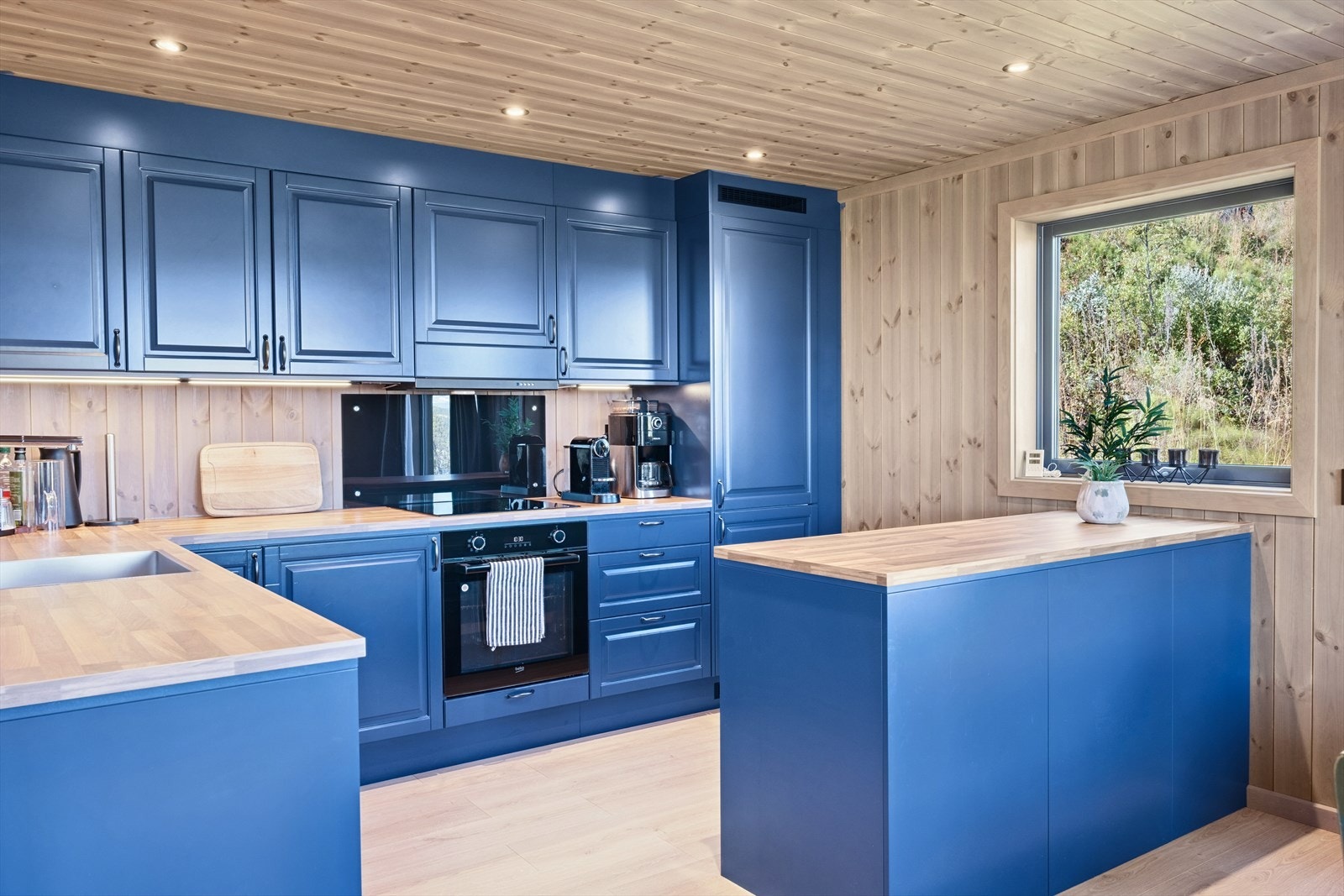 Kjøkkeninnredningen er i folierte plater med over- og underskap, malt i en dyp og moderne blåfarge. Galleribilde