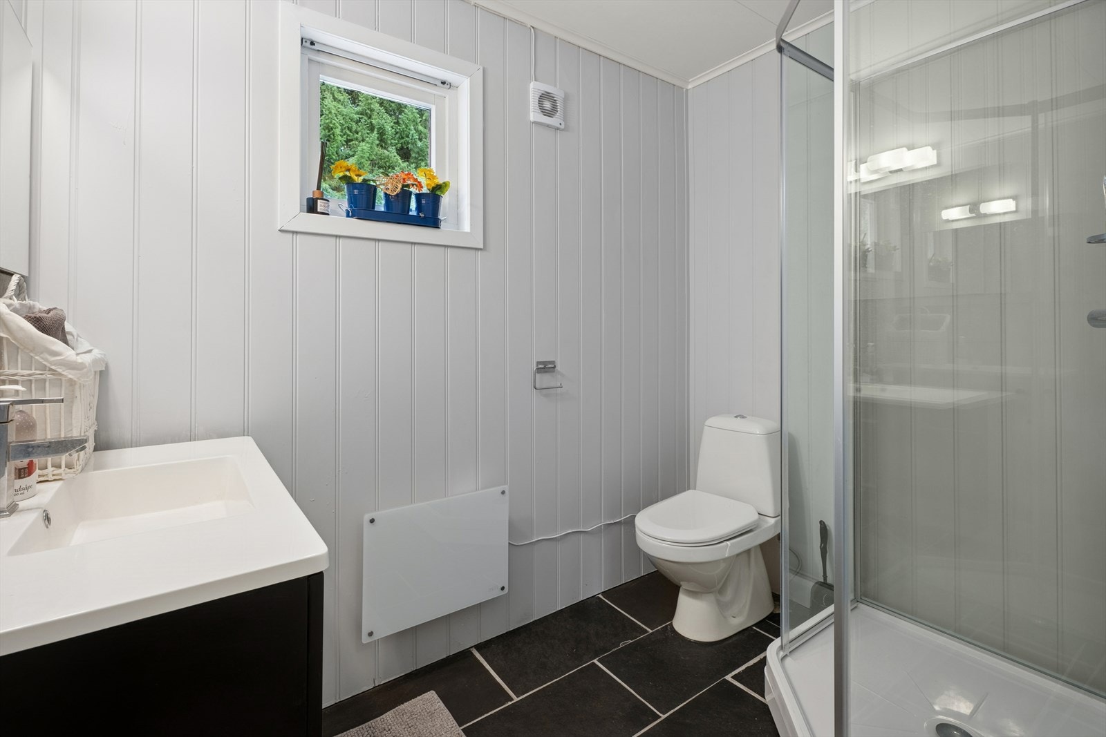 Baderom 2 er av eldre dato og har behov for oppgradering. Det har flislagt gulv og vegger med panelplater, og er utstyrt med klosett, dusjkabinett (montert i 2023) og servant med underskap. Galleribilde