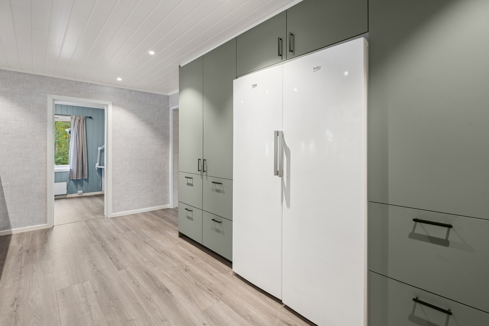 Kjøkkeninnredningen har glatte fronter og en benkeplate med nedfelt vask og kjøkkenkran. Galleribilde