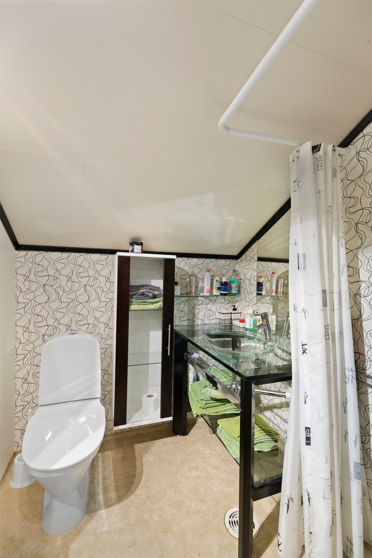 Badet i loftsetasjen har belegg på gulv og tapet på vegger. Rommet er utstyrt med toalett, åpen dusjløsning og baderomsinnredning. Galleribilde