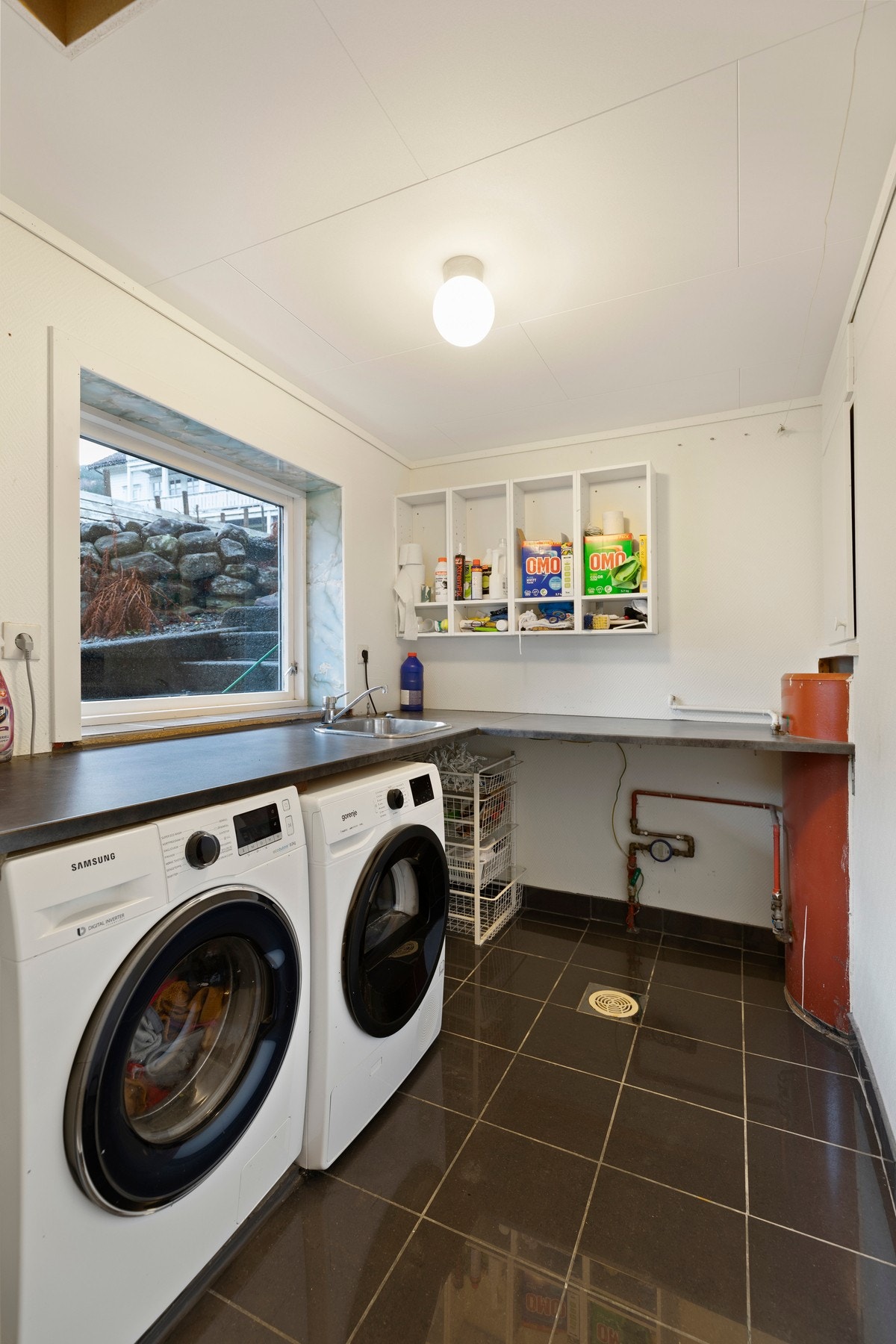 Vaskerommet ble modernisert i 2018 og har flislagt gulv og malt tapet på vegger. Her er varmekabler i gulv, varmtvannsbereder, utslagsvask og opplegg for vaskemaskin/tørketrommel. Galleribilde