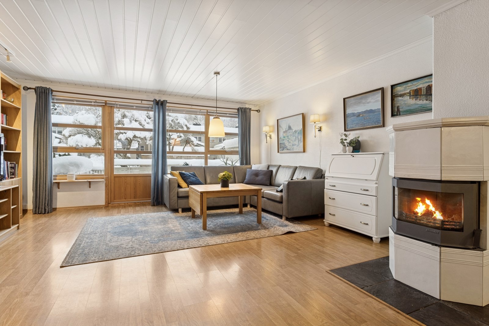 Store vindusflater gir godt med naturlig lys i stuen, og vedovnen sørger for jevn varme. Galleribilde