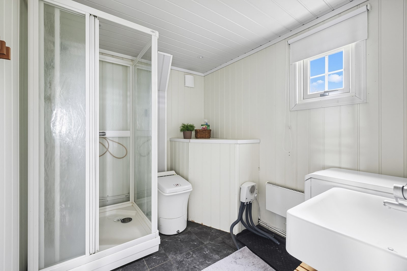 Bad av fin størrelse med laminat på gulv og panel på vegger. Rommet er innredet med servant, dusjkabinett og forbrenningstoalett Galleribilde