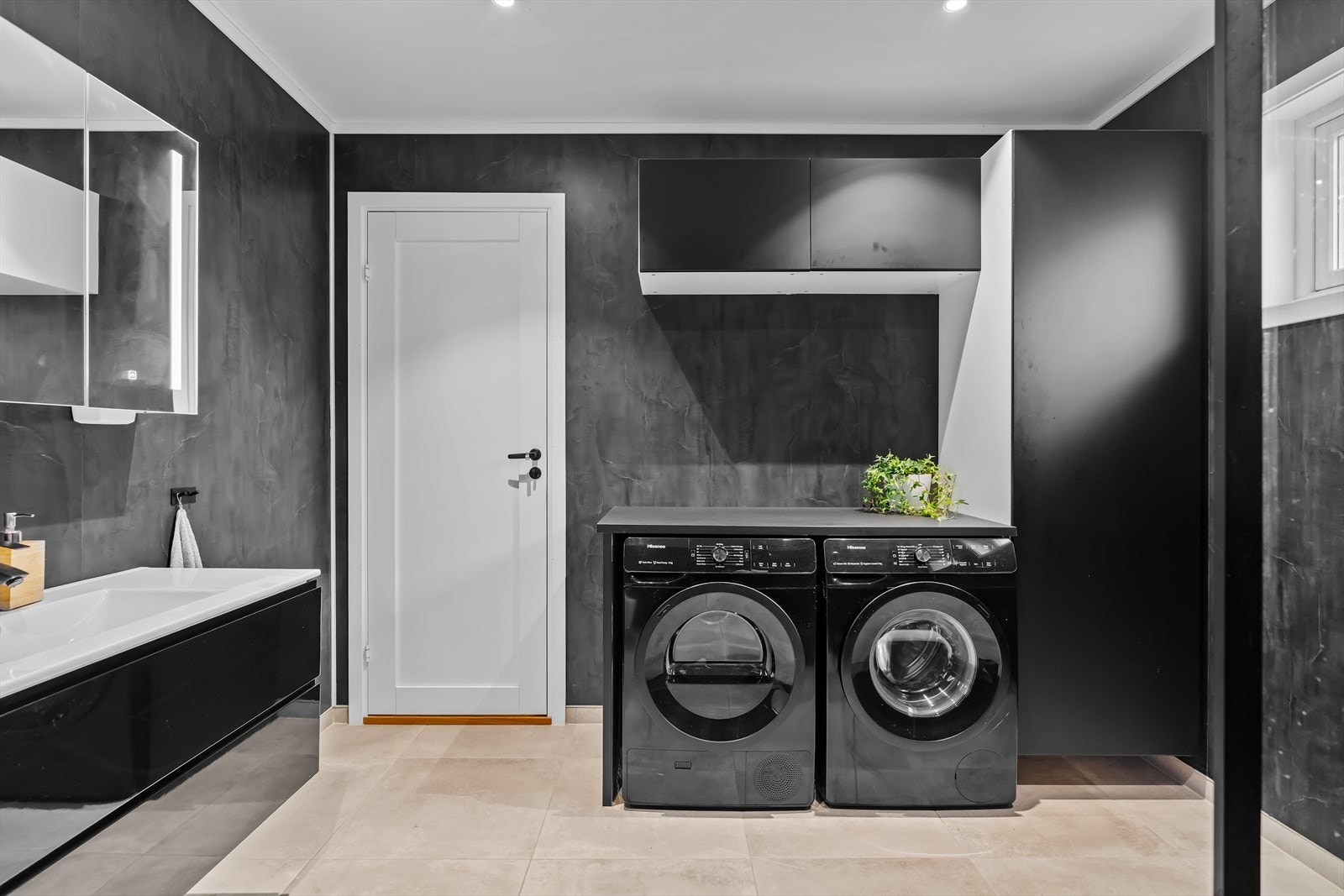 Et funksjonelt bad med opplegg for vaskemaskin og tørketrommel, kombinert med skapplass og arbeidsbenk som gjør hverdagen enklere. Galleribilde