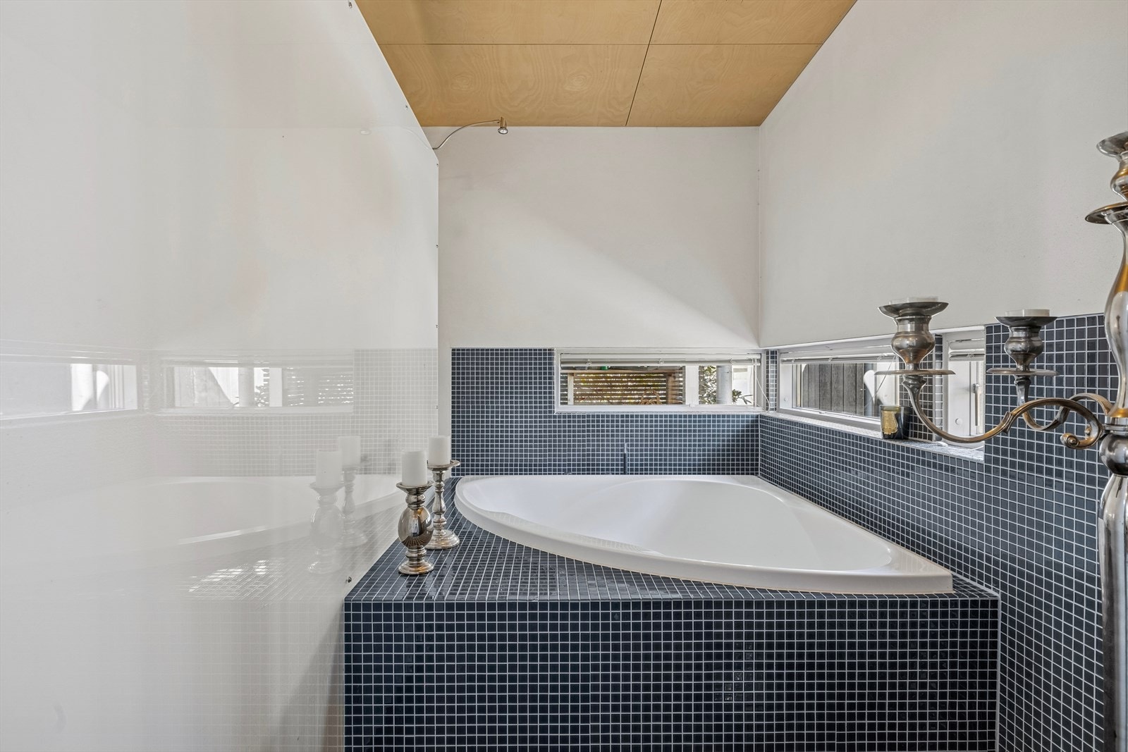 Innebygd badekar med stilfull flislagt sokkel, omgitt av lune detaljer og naturlig lys fra vinduet - en perfekt plass for avslapning. Galleribilde