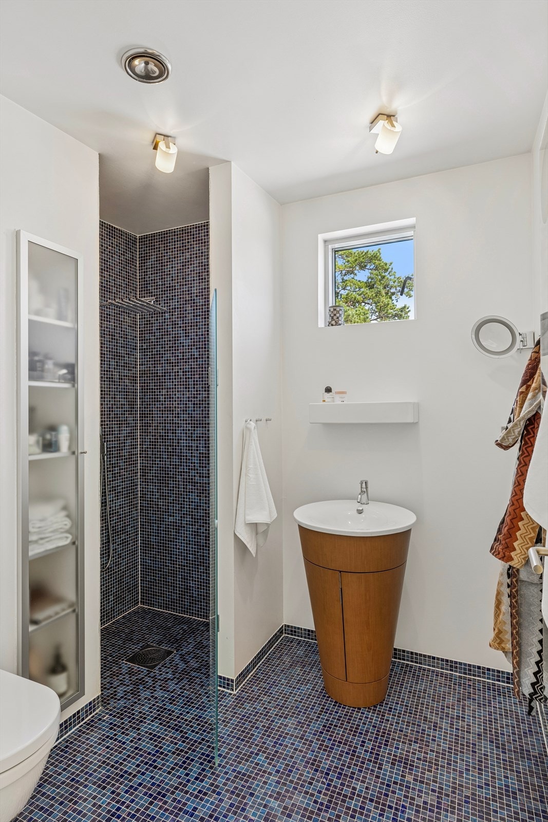 Baderommet er innredet med fliser på gulv og i dusjsonen, og har baderomsmøbel med servant, dusjnisje og vegghengt toalett. Galleribilde