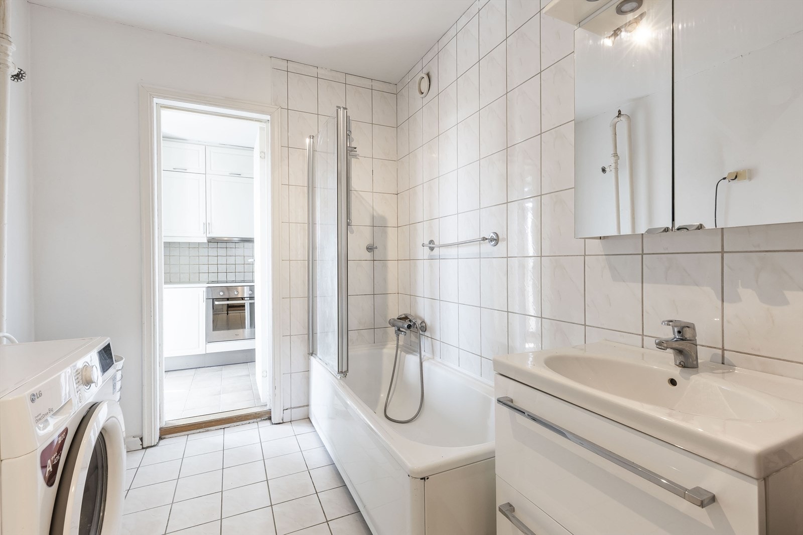 Flislagt bad med innredning, speilskap, badekar m/dusj og opplegg til vaskemaskin Galleribilde