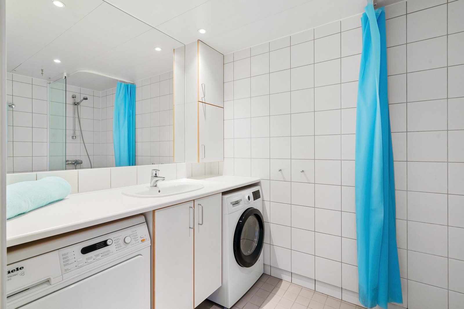 Baderommet har innredning med nedfelt servant, veggmontert toalett, dusjvegger/hjørne og opplegg for vaskemaskin og tørketrommel. Galleribilde