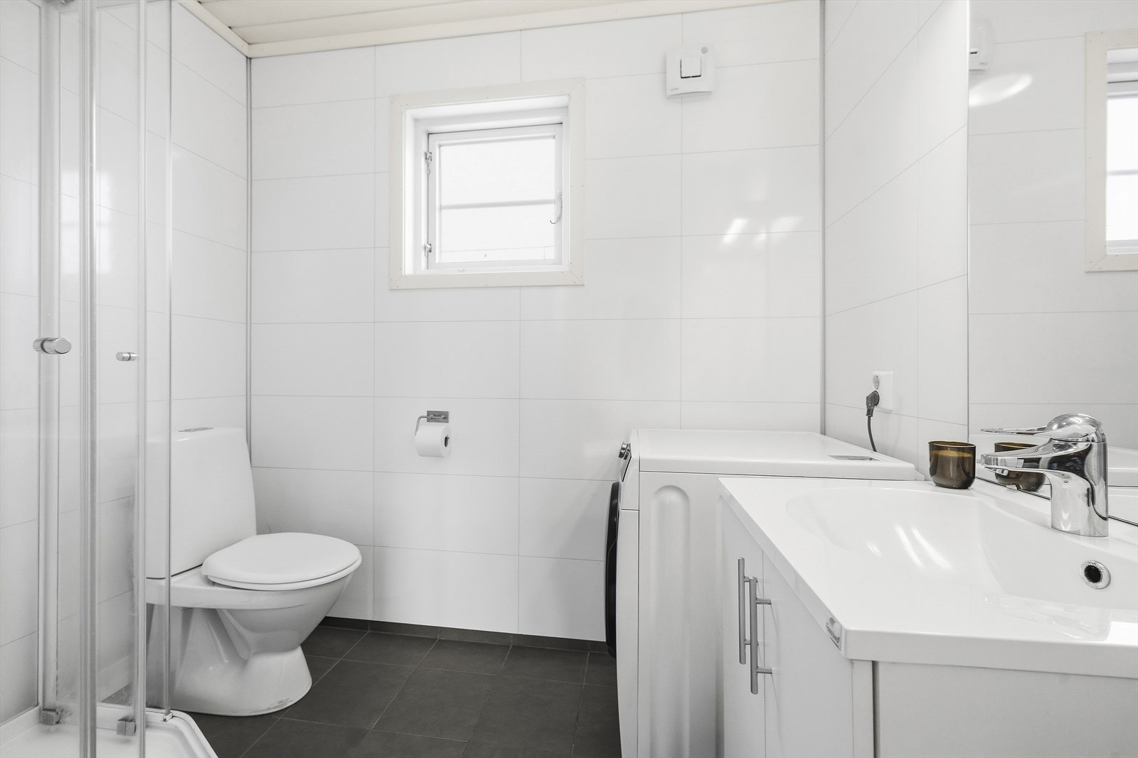 Badet er utstyrt med servant over skapinnredning, toalett, dusjkabinett og opplegg til vaskemaskin Galleribilde