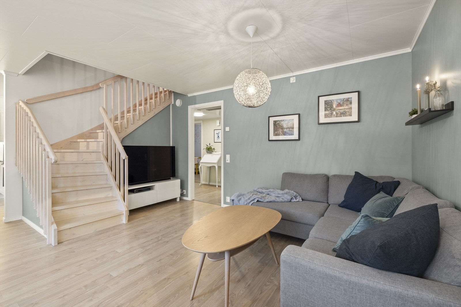 Pen stue med laminat på gulv og slette vegger malt i et moderne fargepalett. Stuen har en pen kontrastvegg malt i en fin blåtone. Galleribilde