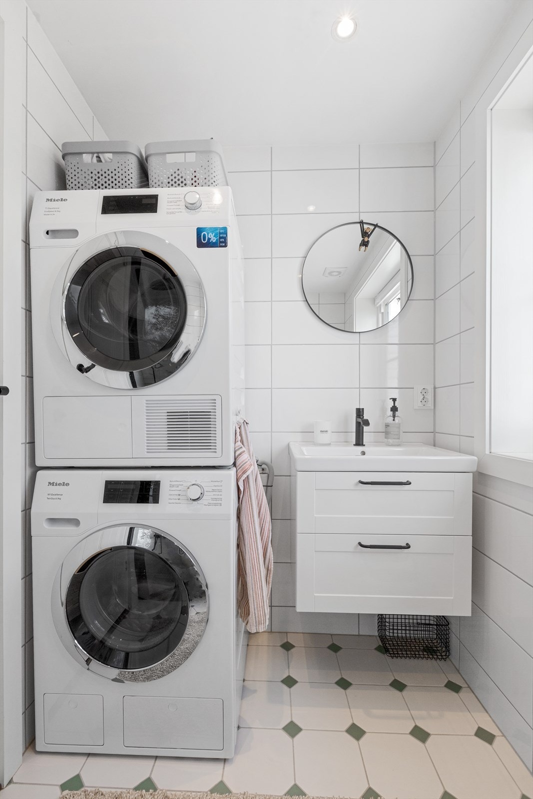 Kombinert bad og vaskerom med plassbesparende vaskemaskin og tørketrommel i søyle. Vegghengt servantskap og speil med belysning. Galleribilde