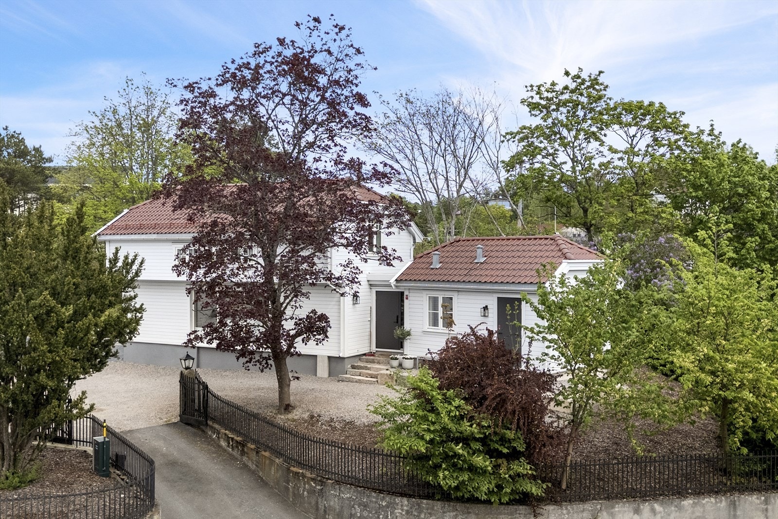 Eiendommen ligger på en solrik og pent opparbeidet tomt, omgitt av frodig vegetasjon, med gruslagt parkeringsplass og klassisk smijernsport. Galleribilde