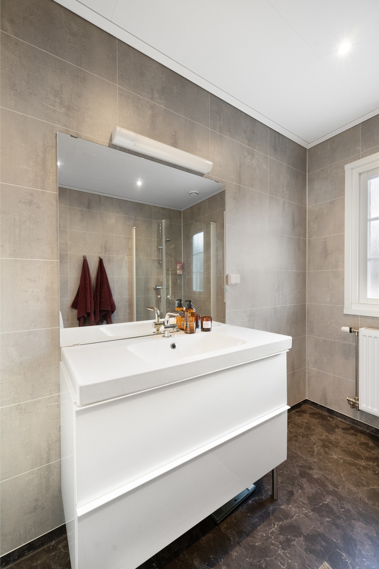 Rommet er innredet med servant med underskap, speil med tilhørende belysning, dusjvegger og gulvmontert wc. Galleribilde