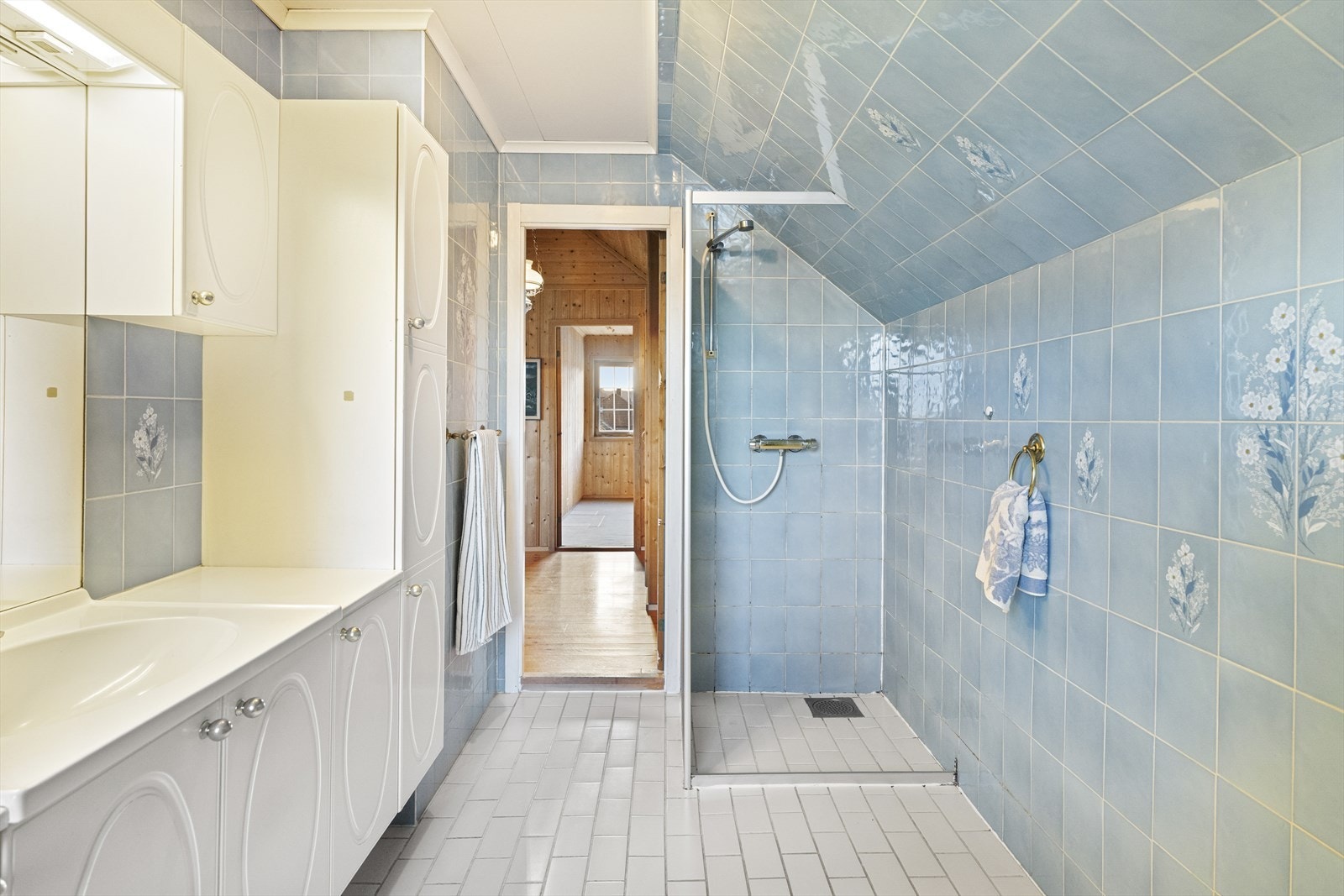 Badet oppe har hvite gulvfliser med varme, mens både veggene og skråtaket er kledd med lyseblå dekorfliser. Galleribilde