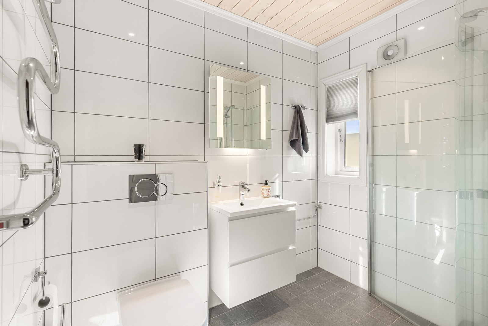 Bad2 er innredet med vegghengt toalett, servant i innredning, dusjhjørne og håndkletørker Galleribilde