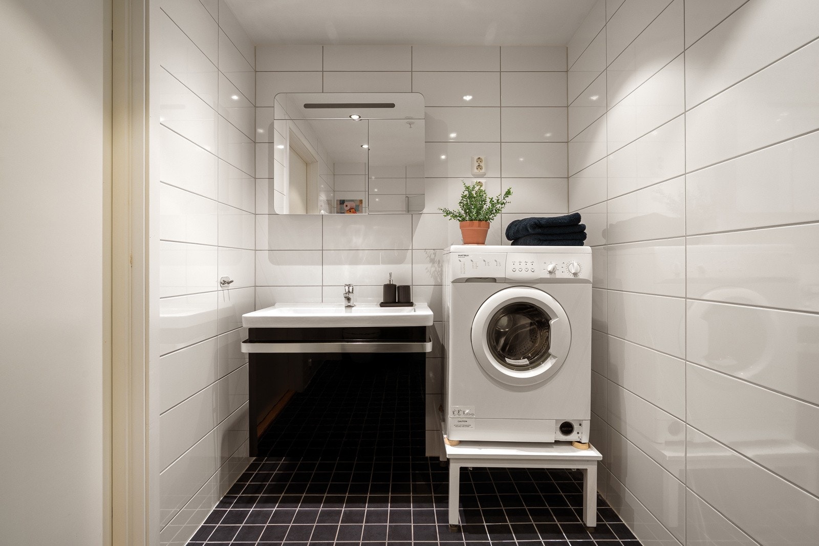 Flott og moderne flislagt bad med stort dusjhjørne, vegghengt wc og opplegg for vaskemaskin.