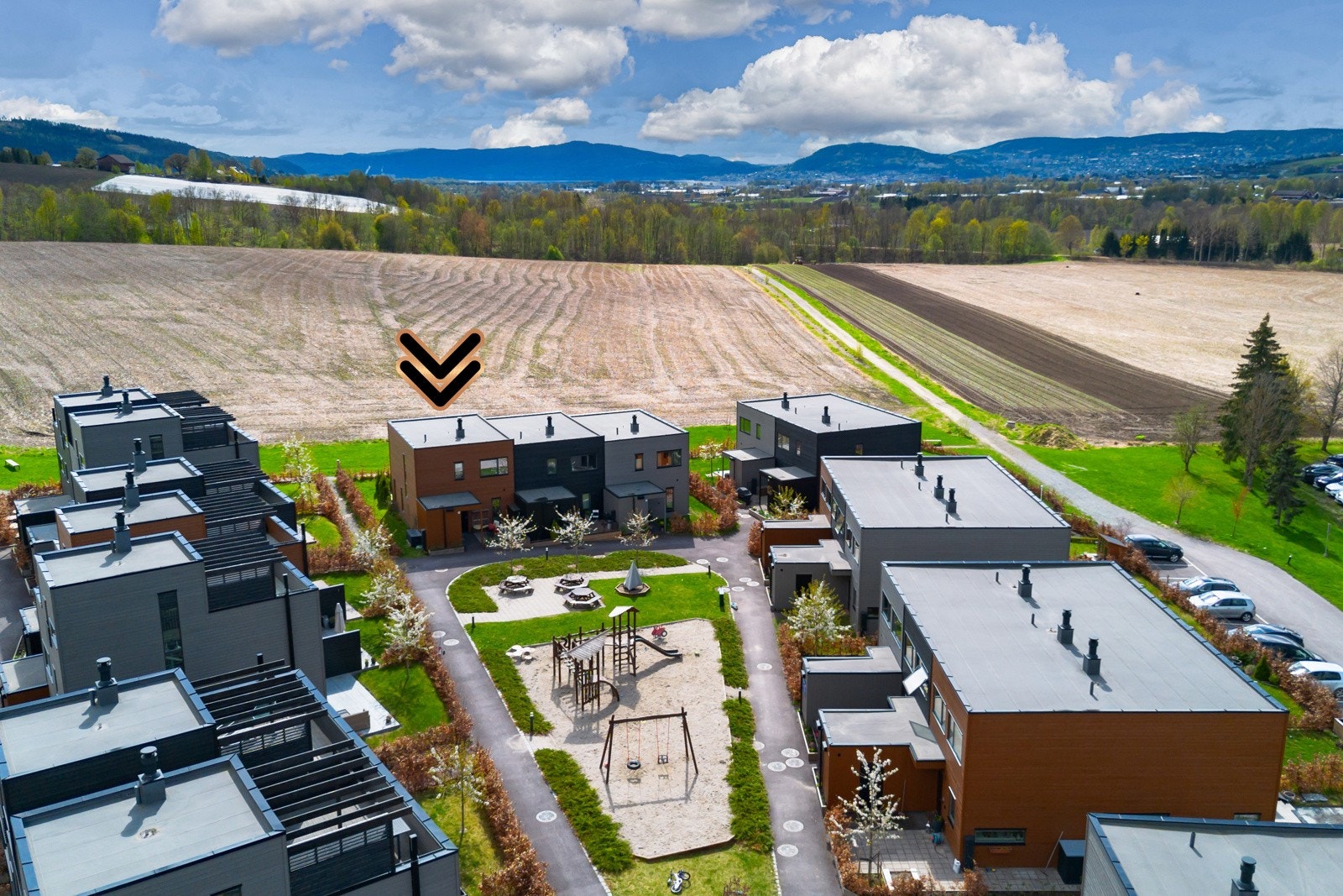 Moderne rekkehus med lekeplass i hage, omkranset av åker og fjellutsikt. Parkeringsmuligheter i carport Galleribilde