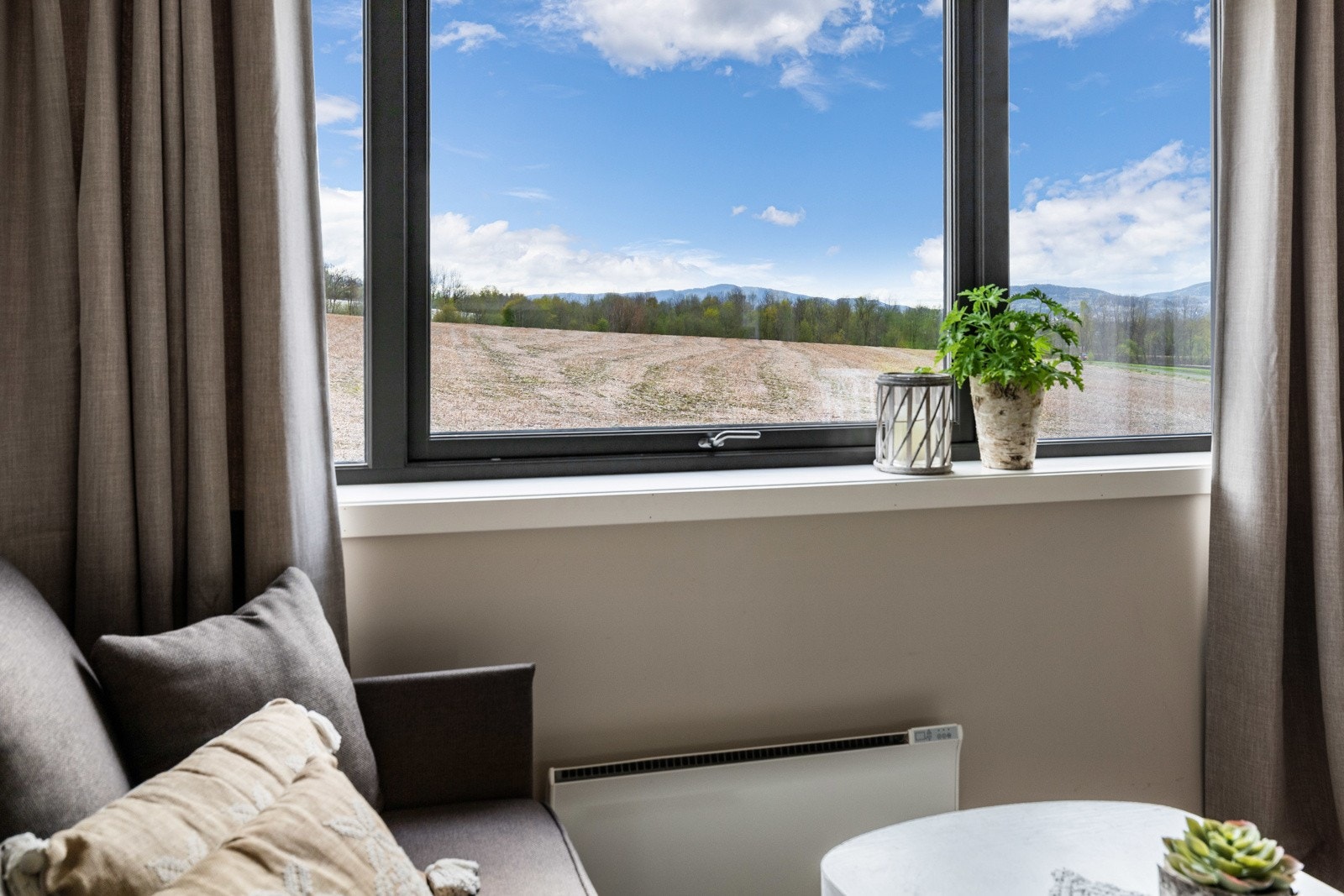 Stort vindu med utsikt over et åpent jorde og åser i bakgrunnen. Galleribilde