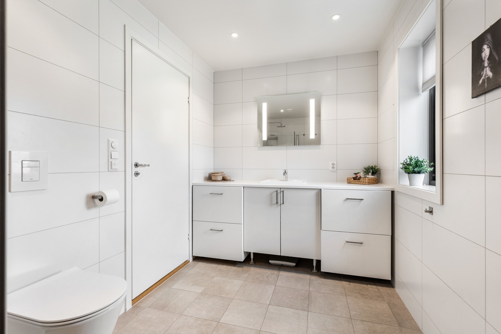 Lyst og romslig baderom med hvite fliser, vegghengt toalett og moderne baderomsinnredning. Galleribilde