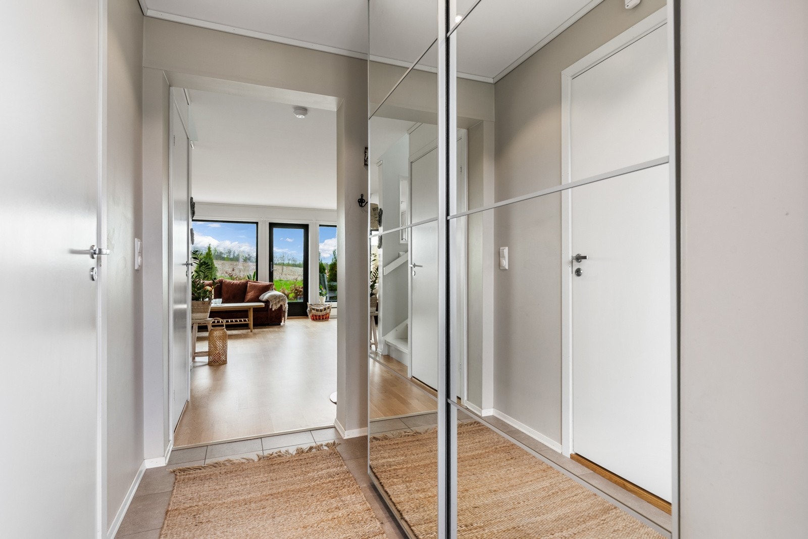 Lys gang med speilskap og utsikt til stue med store vinduer. Galleribilde