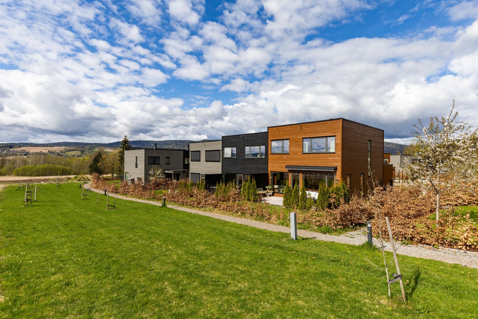 Moderne rekkehus med store vindusflater og treverk, plassert i et åpent og grønt område med utsikt til åsene. Galleribilde