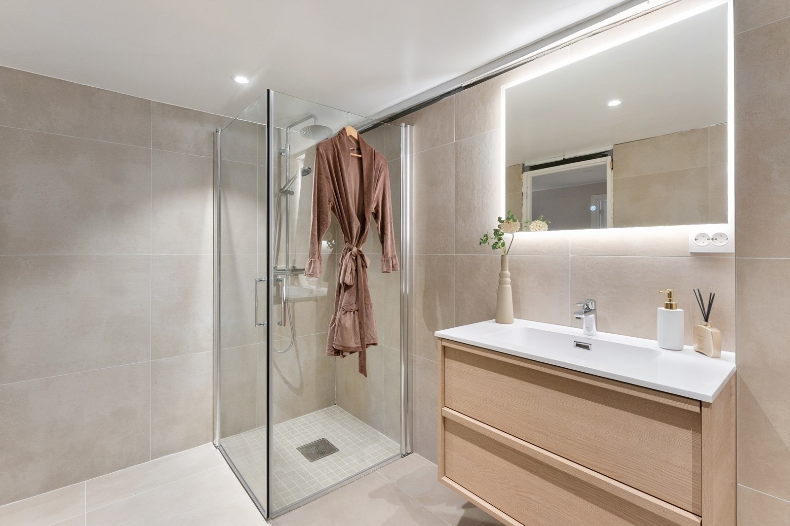 Badet er fra 2025 med flislagt gulv med varmekabler, speil med LED lys over servant, vegghengt toalett og elektrisk styrt vifte. Galleribilde