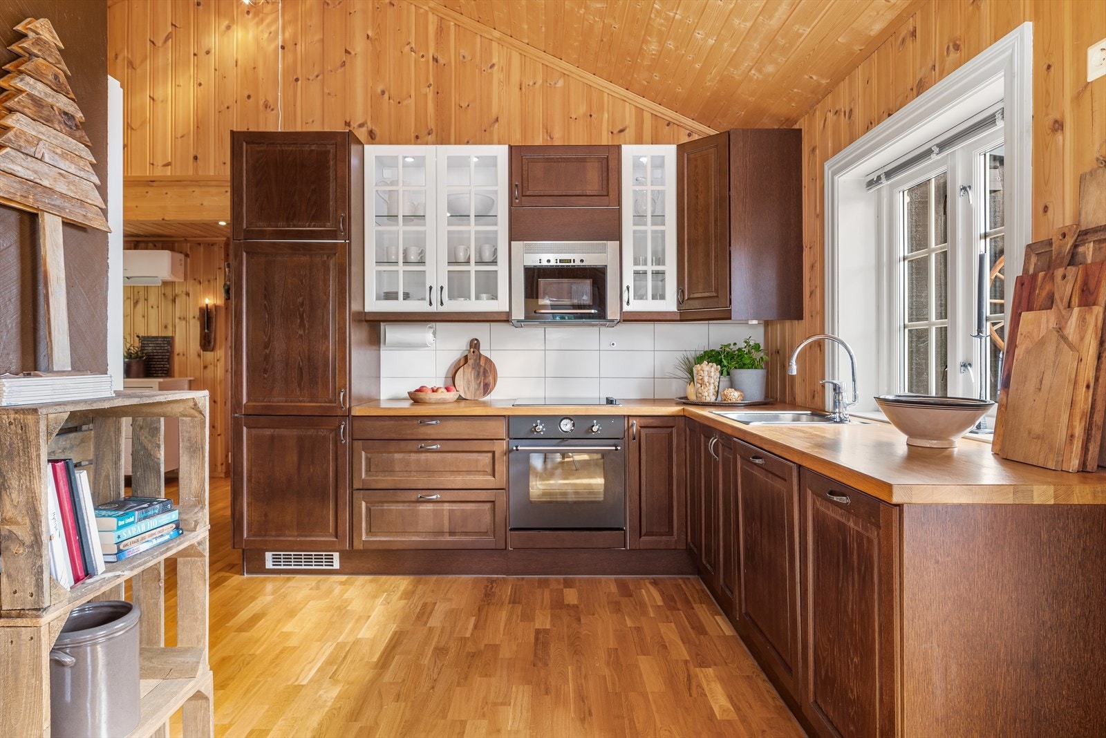 Kjøkkeninnredningen har profilerte fronter, hvite vitrineskap og benkeplate med nedfelt oppvaskkum. Galleribilde