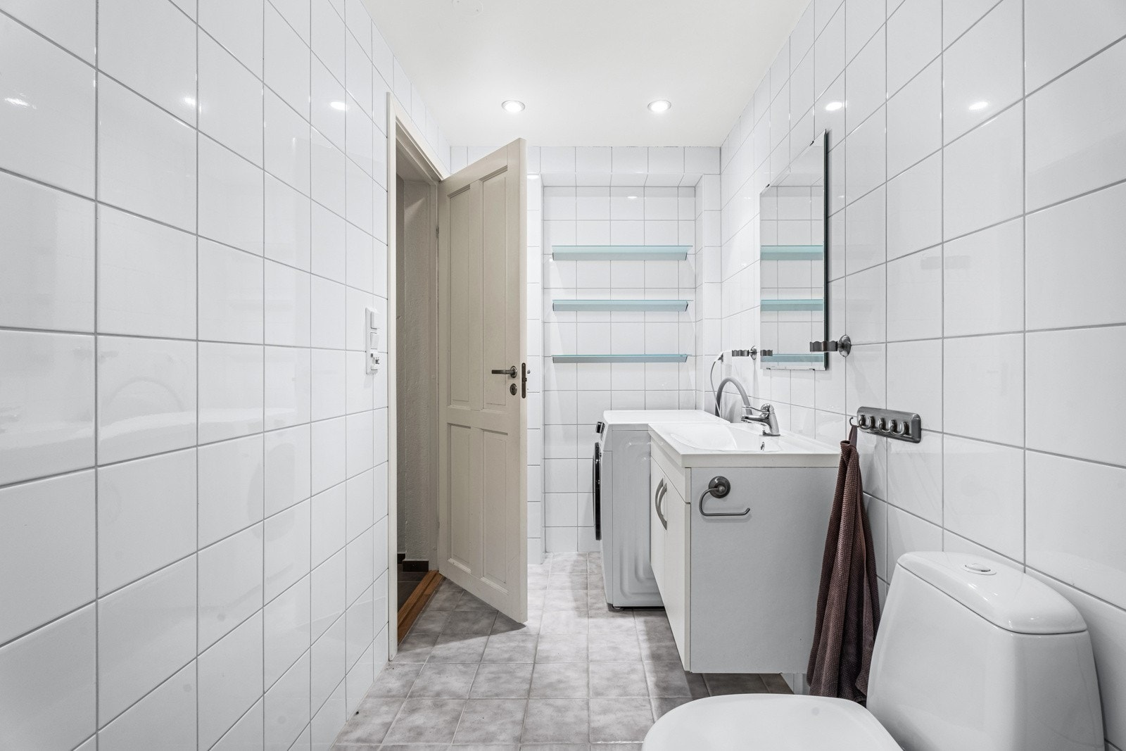 Veggmontert servantinnredning med heldekkende vask og ett-greps armatur i krom, gulvstående klosett og opplegg for vaskemaskin Galleribilde