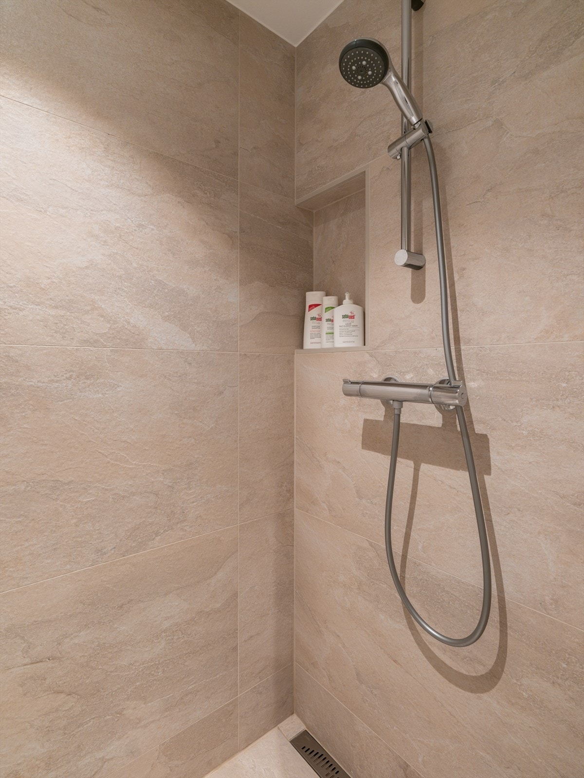 Dusjsonen har en praktisk nisje for oppbevaring og en moderne slukrenne. Galleribilde