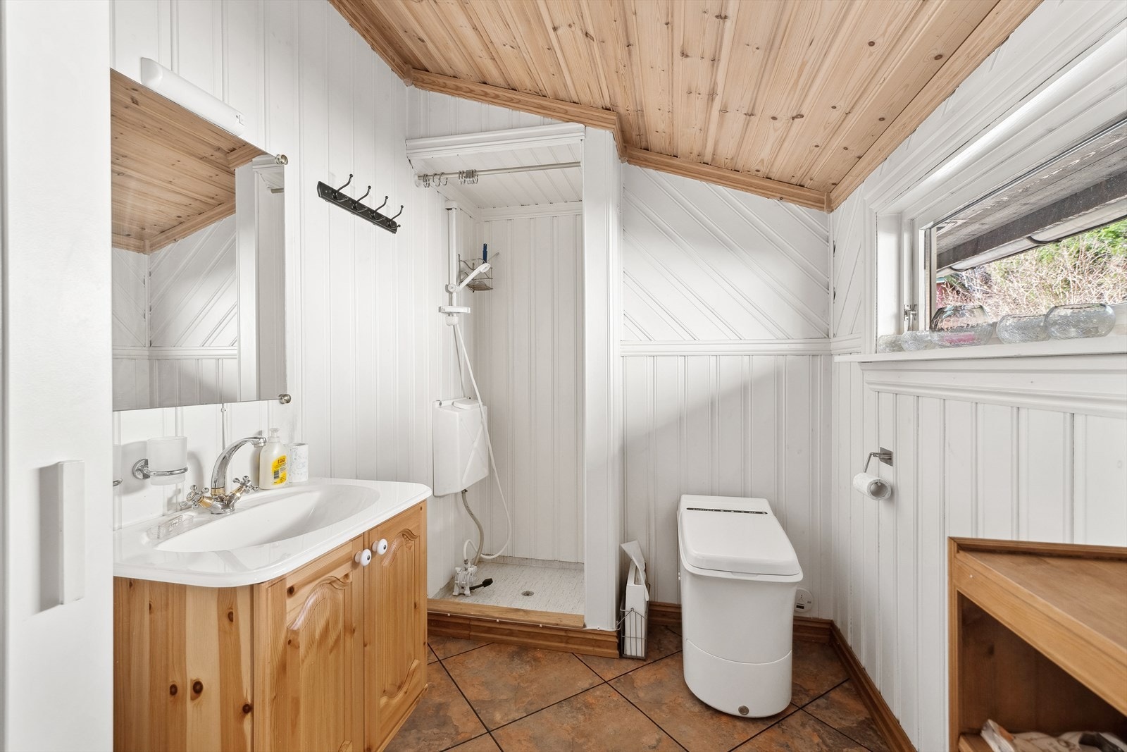 Bad med Cinderella forbrenningstoalett, servant med slange fra plastkanne og 12 volts pumpe, panelt dusjnisje med vanntank og fotpumpe. Galleribilde