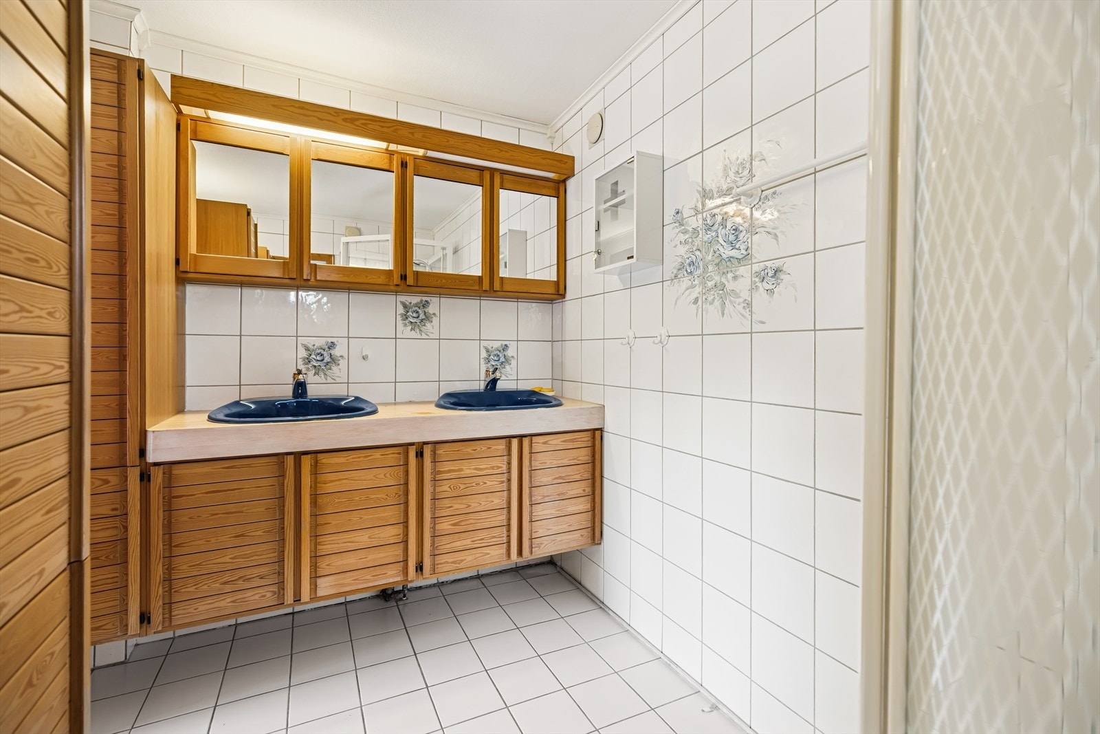 Bad i kjeller med flislagt gulv og vegger av panel og fliser i våtsonen. Rommet er utstyrt med servantinnredning, toalett, dusjkabinett og opplegg for vaskemaskin. Galleribilde