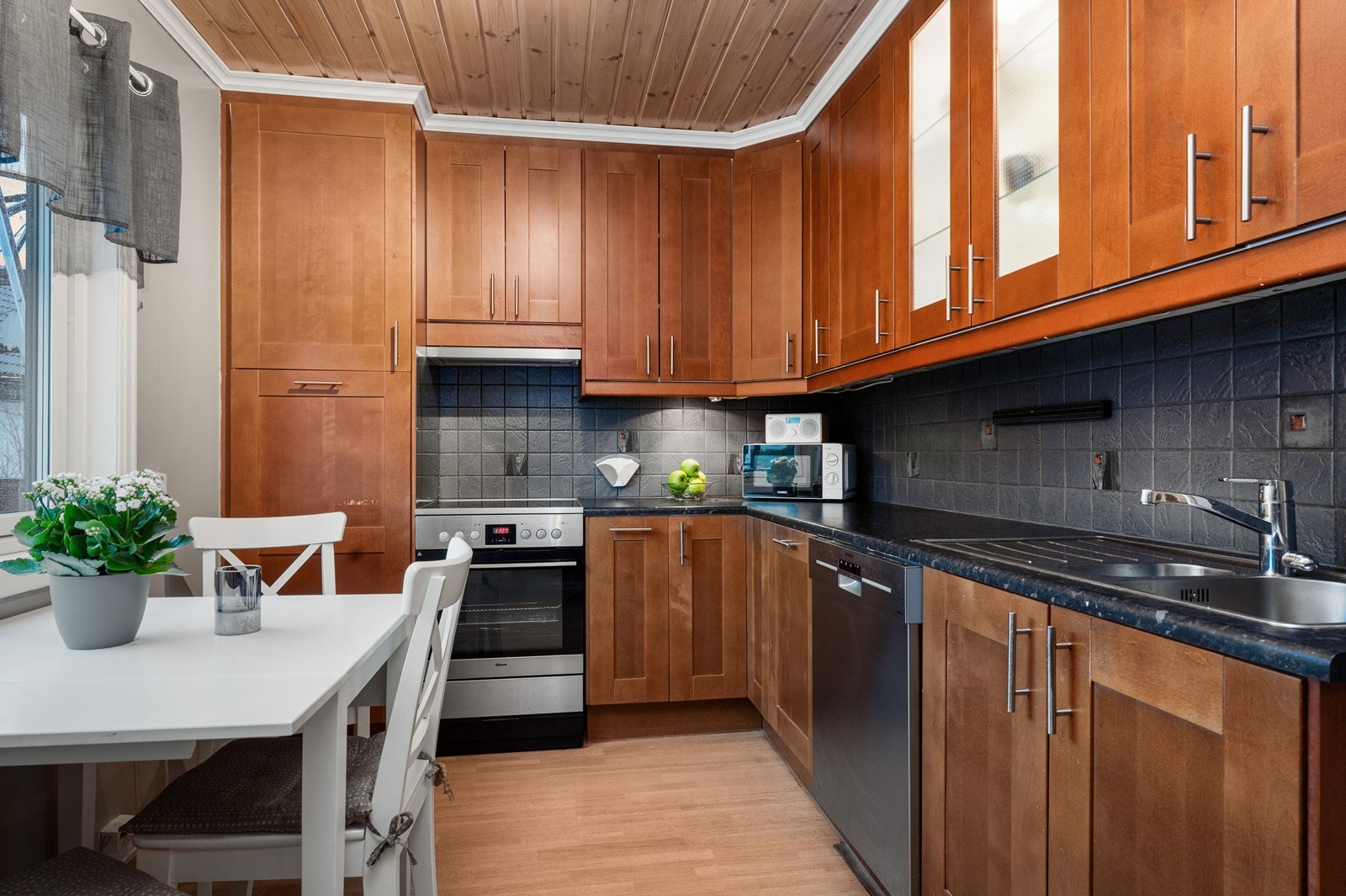 Kjøkkenet har en praktisk innredning med trefronter og mørk benkeplate. Oppvaskmaskin og komfyr gir funksjonelle løsninger. Galleribilde