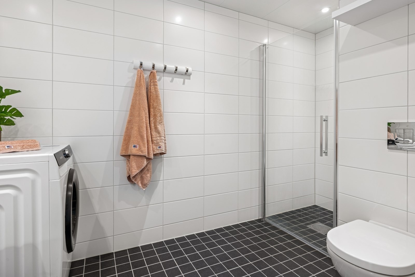 Badet er innredet med et veggmontert toalett, baderomsinnredning med heldekkende servant, speil, dusjnisje og opplegg for vaskemaskin. Galleribilde