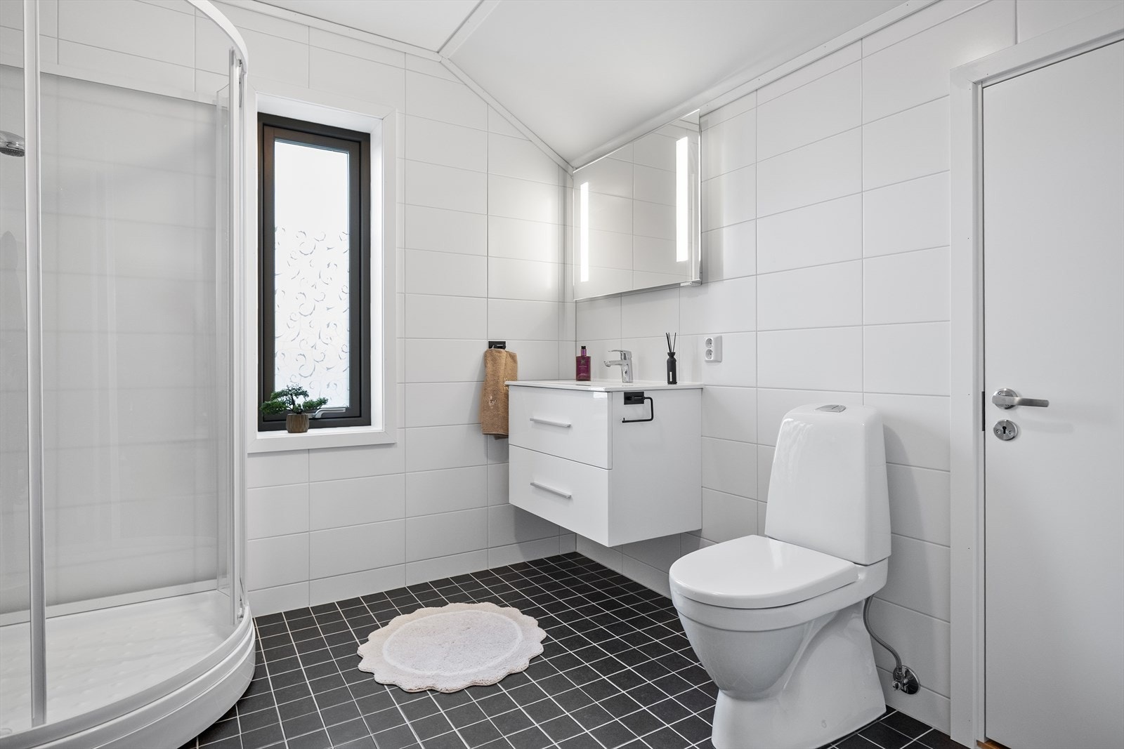 Badet i 2. etasje med dusjkabinett, toalett, servant med skuffinnredning og speil med lys. Galleribilde