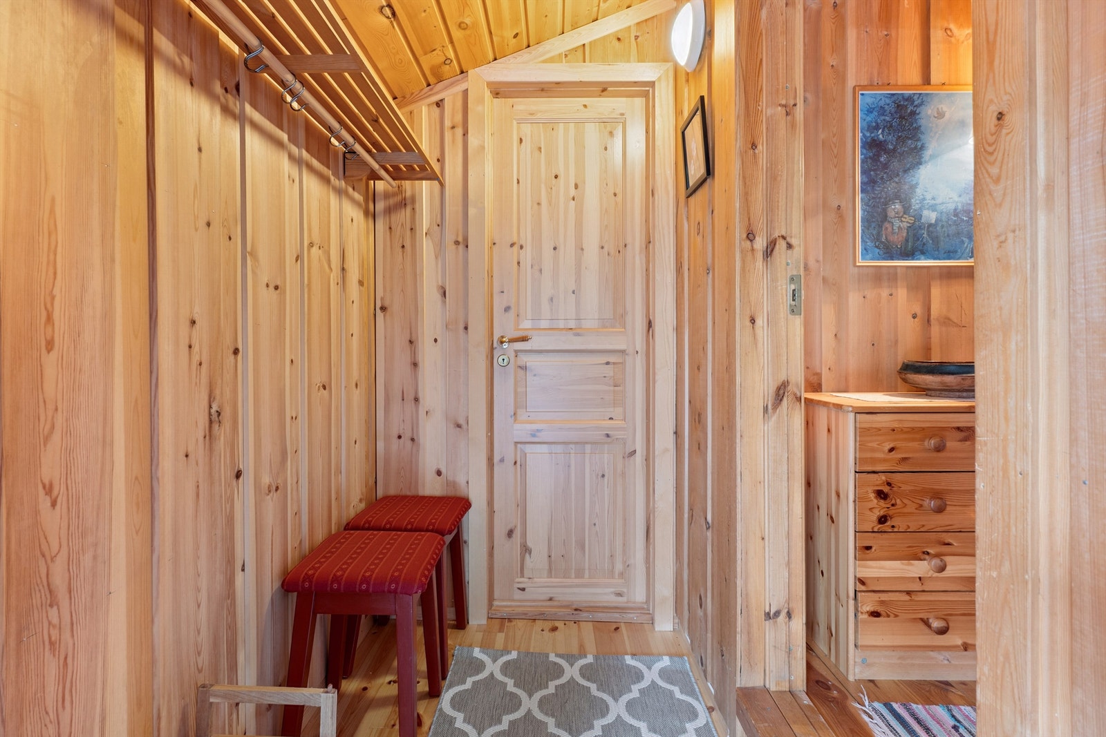 Vi trer inn i en praktisk entré med furugulv og trepanel, som er gjennomgående i hytta. Galleribilde