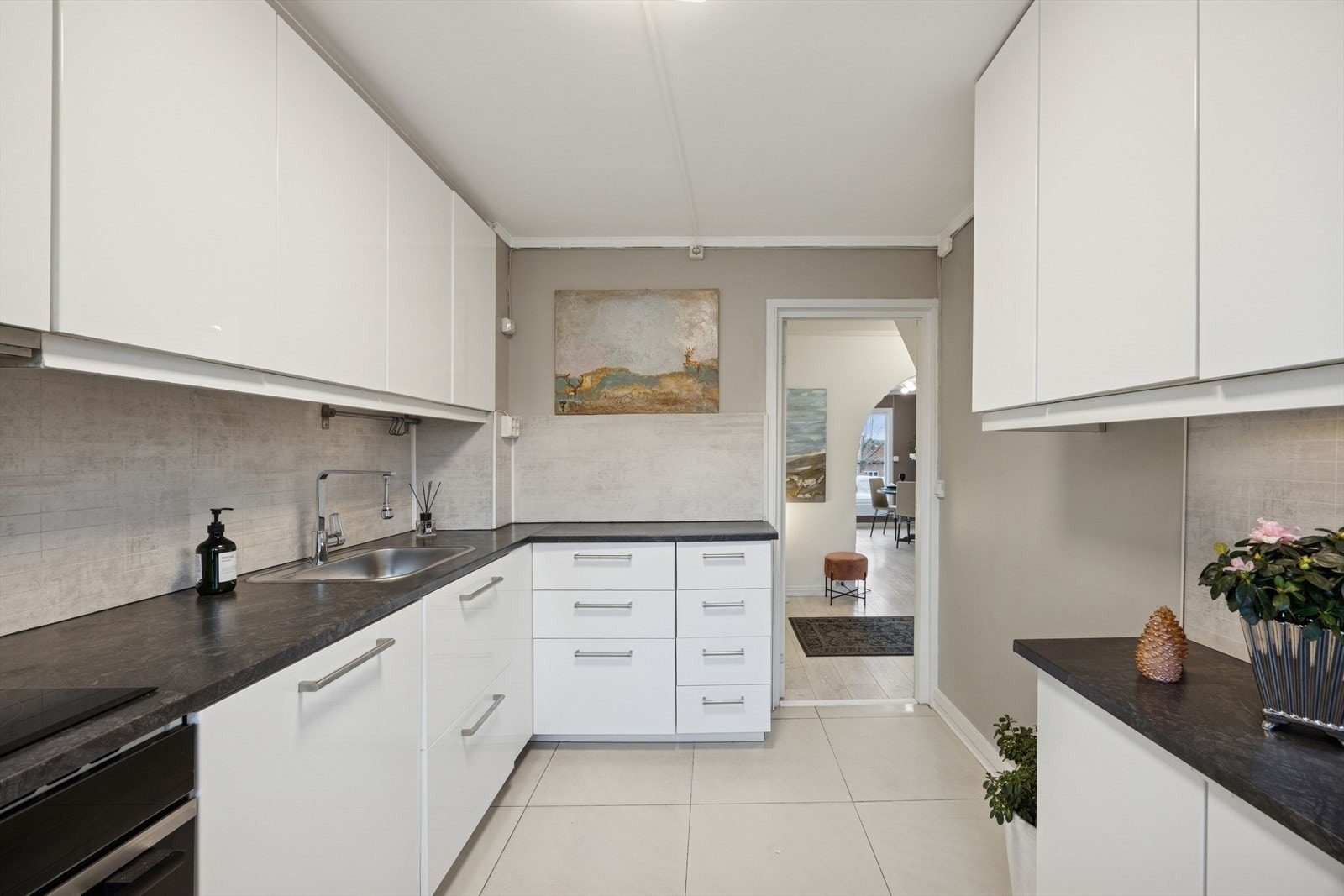 Kjøkkeninnredning fra IKEA med slette høyglans fronter, laminat benkeplate med flisplater på bakvegg, rustfri oppvaskkum, ventilator med utluft og innfelte hvitevarer som stekeovn, induksjonsplatetopp,
oppvaskmaskin og kjøleskap Galleribilde