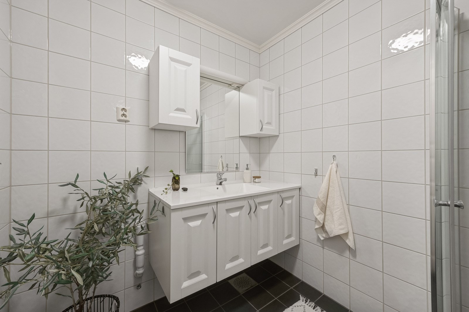 Flislagt bad med hvit innredning, dusjhjørne og opplegg for vaskemaskin Galleribilde