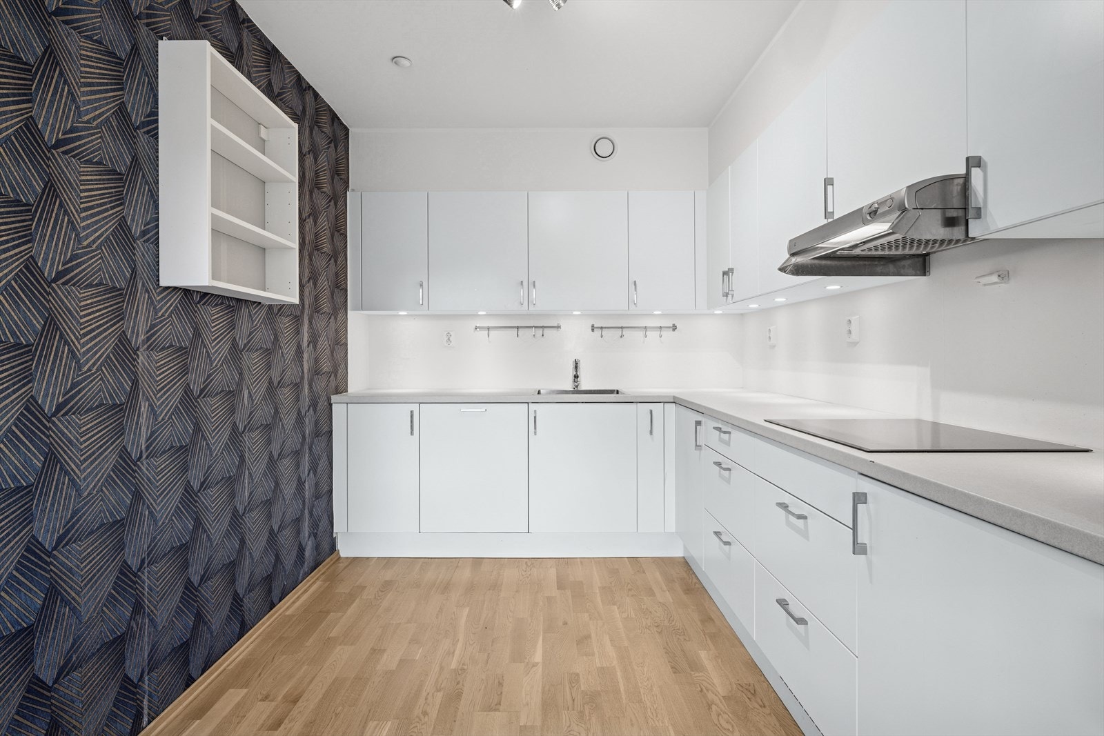 Kjøkkeninnredning fra Arens med slette fabrikklakkerte fronter, laminat benkeplate, enkel oppvaskkum, ventilator og integrert stekeovn, koketopp, oppvaskmaskin og kjøl-/fryseskap. Galleribilde