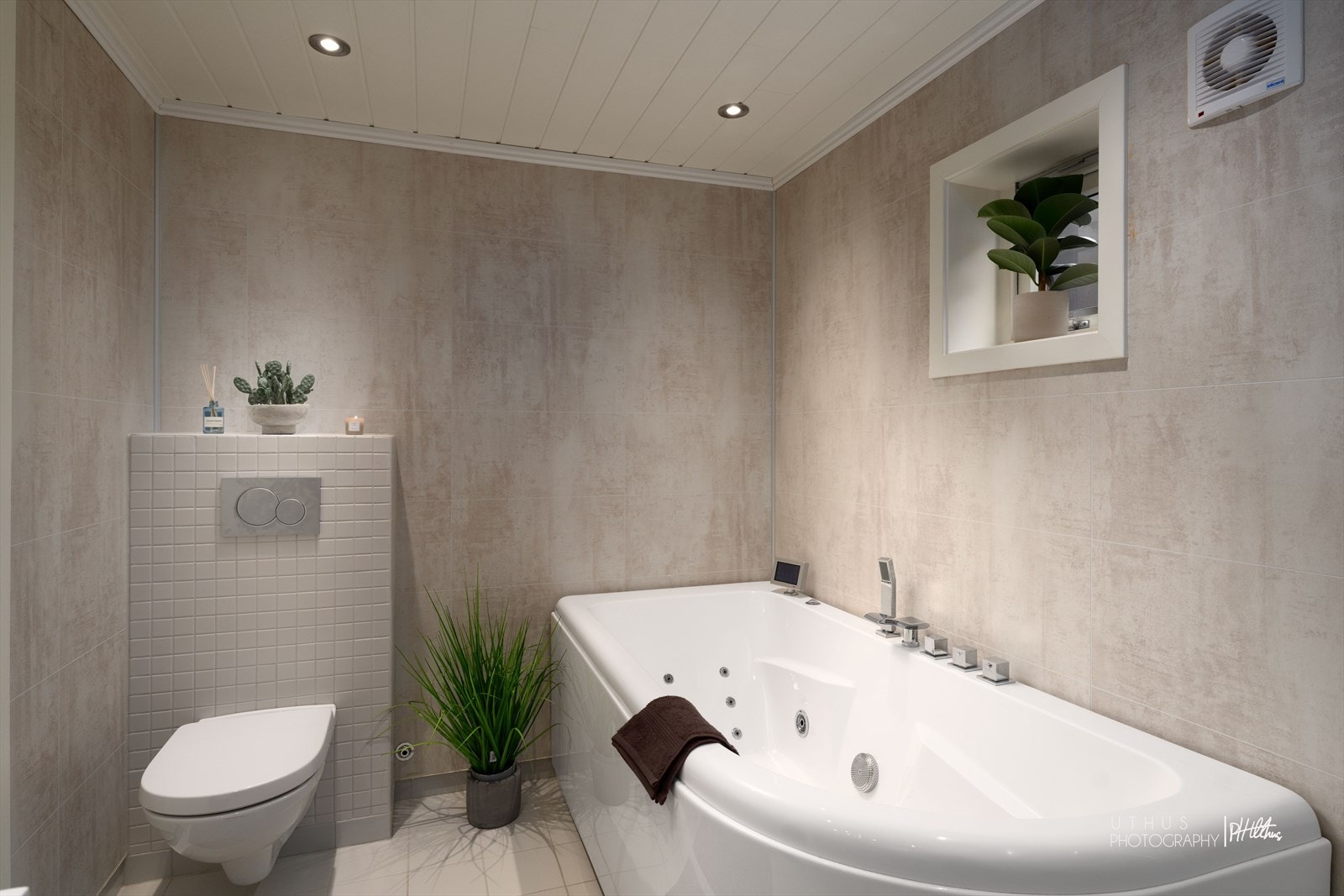 Baderommet er innredet med en nedfelt servant, overhengende speil og belysning. Dusjen er plassert i hjørnet og har håndholdt dusjarmatur. Videre er det montert et vegghengt toalett og badekar. Galleribilde