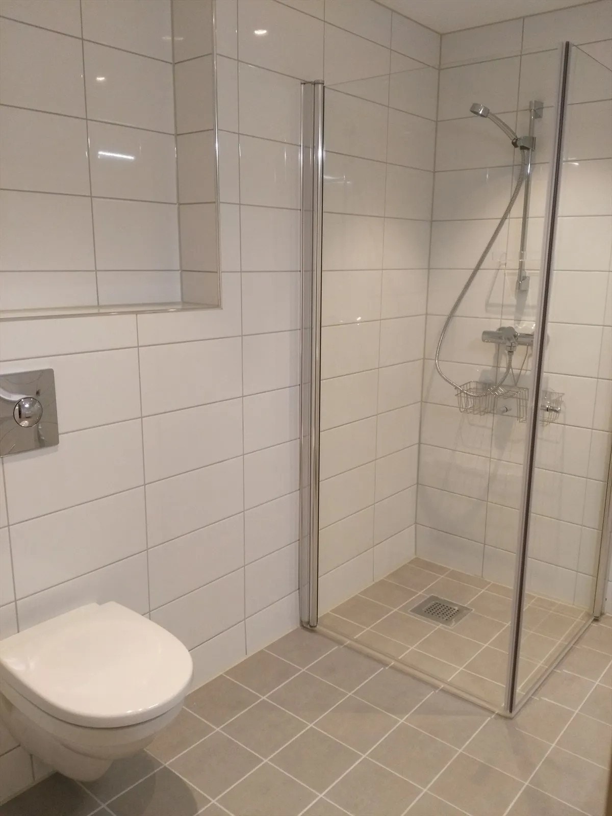 Lekkert flislagt bad med vegghengt toalett, dusjhjørne og servant m/innredning. Galleribilde