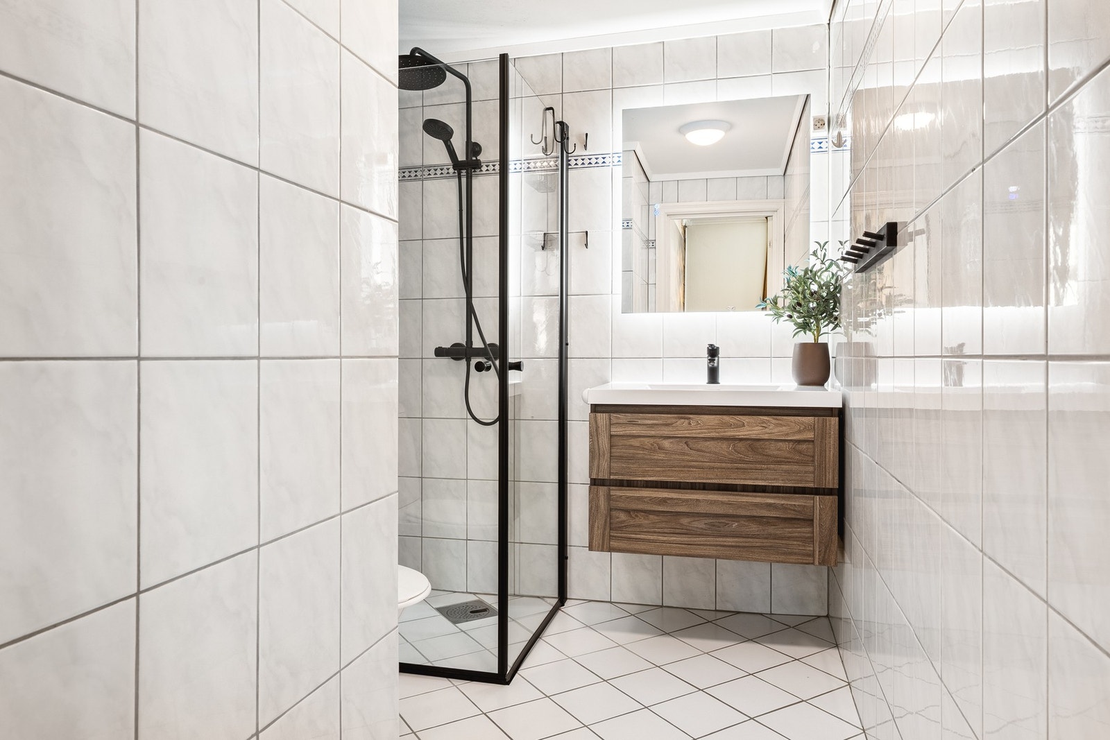 Badet er helfliset og utstyrt med dusjhjørne, servant med skuffer og toalett. Galleribilde