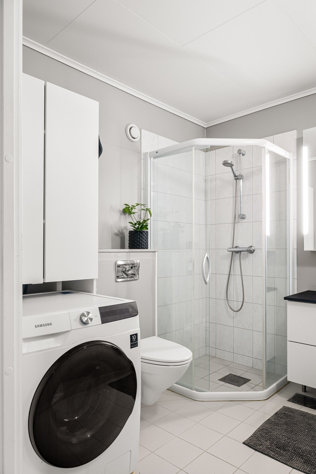 Innredet med servant i baderomsmøbel, dusjhjørne og vegghengt toalett. Det er opplegg for vaskemaskin. Galleribilde