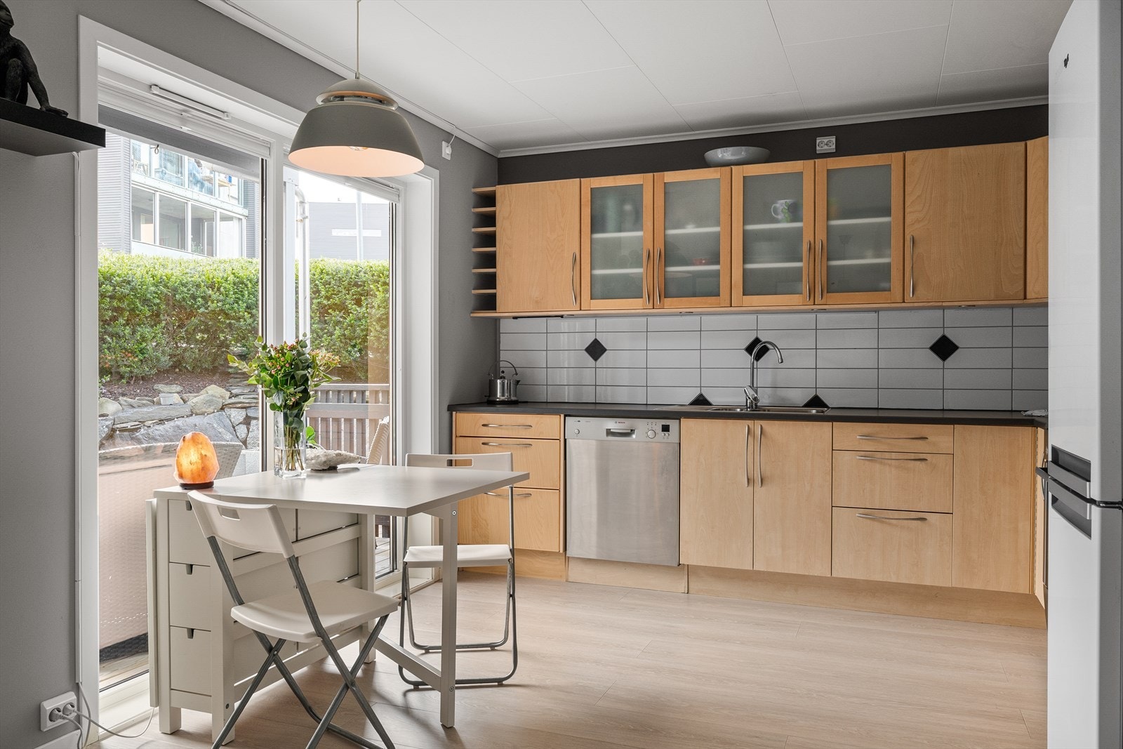 Kjøkkeninnredning fra byggeår med lyse, slette fronter, samt praktisk backsplash over kjøkkenbenken. Galleribilde