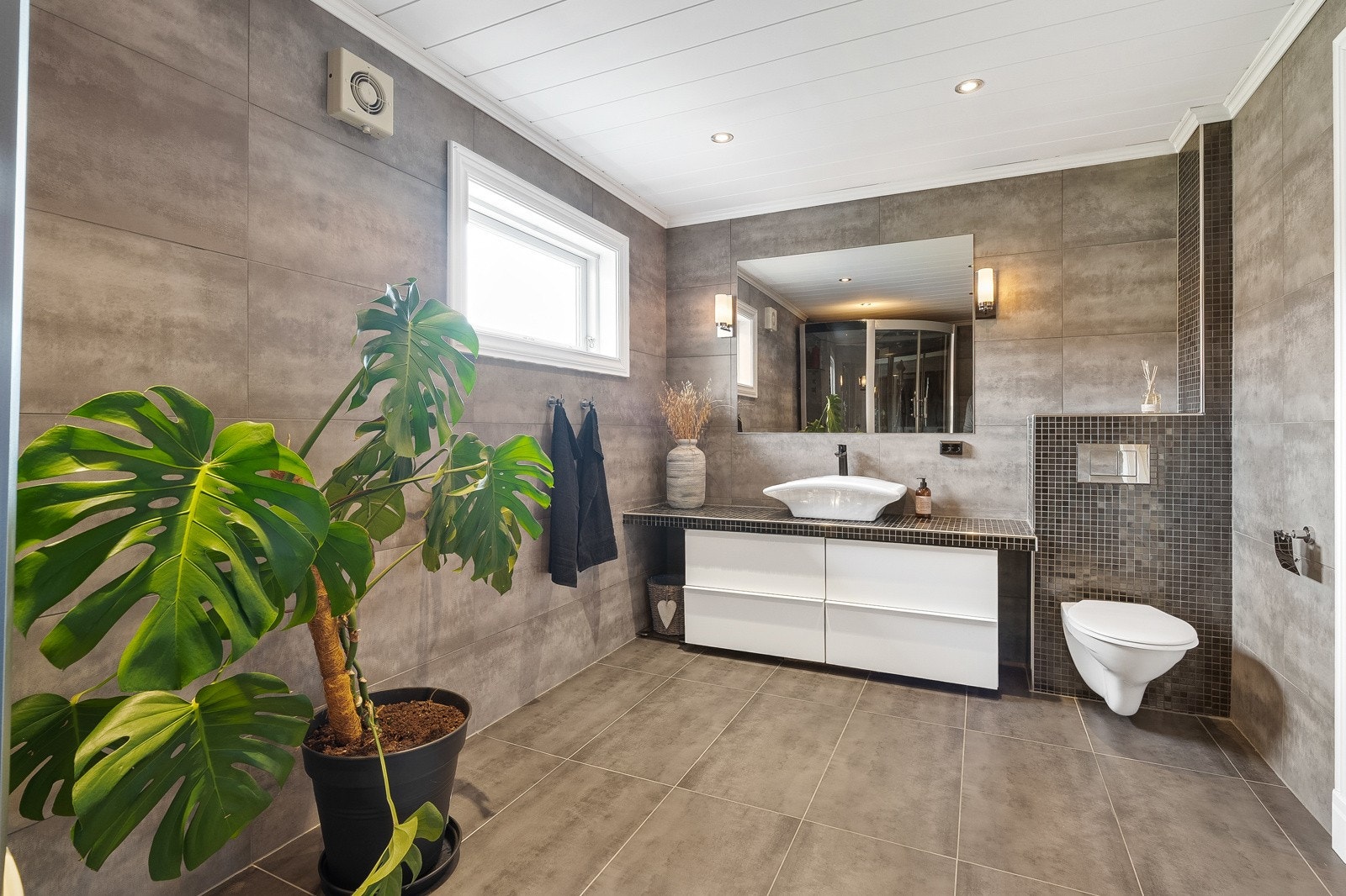 Delikat bad fra 2013. Lekkert uttrykk med moderne fliser, vegghengt toalett og innredning med rene linjer. Galleribilde