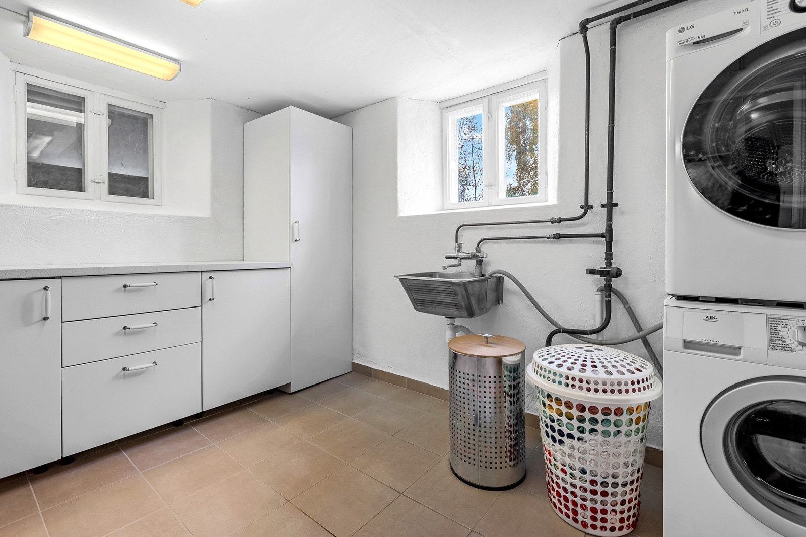 Praktisk og romslig vaskerom med flislagt gulv, innredning, utslagsvask og plass til vaskemaskin og tørketrommel. Galleribilde