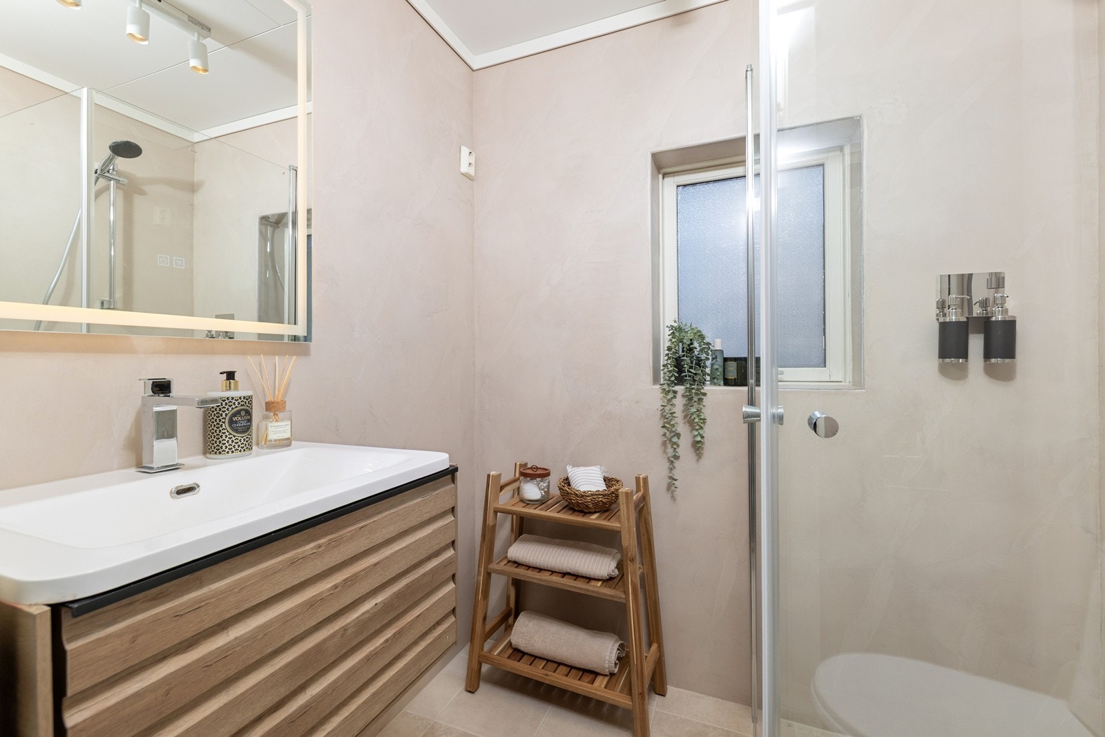 Baderomsinnredningen har heldekkende nedfelt servant og rom for oppbevaring i skuffeseksjon, det er speil med LED belysning. Videre har badet dusj med dusjvegger og toalett. Opplegg for vaskemaskin. Galleribilde