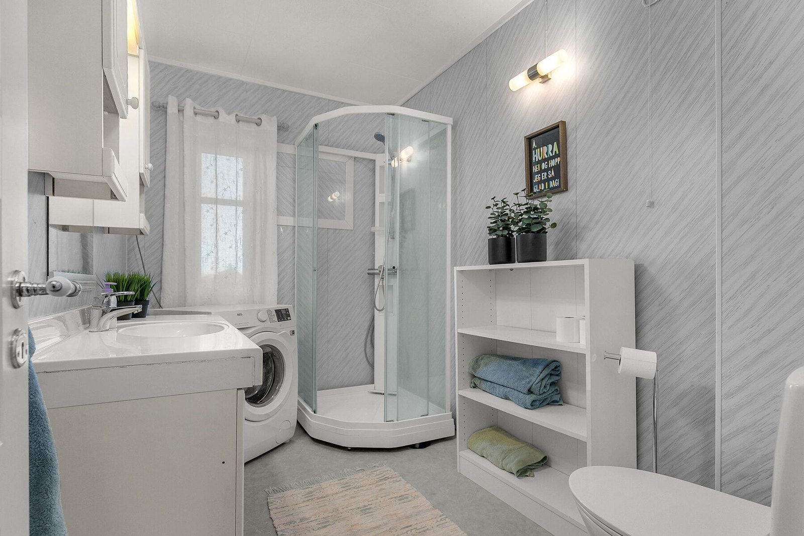 Bad med belegg på gulv, baderomsplater på vegger. Malte plater i tak. Baderomsinnredning med hvite profilerte fronter. Dusjkabinett, toalett og opplegg til vaskemaskin. Galleribilde